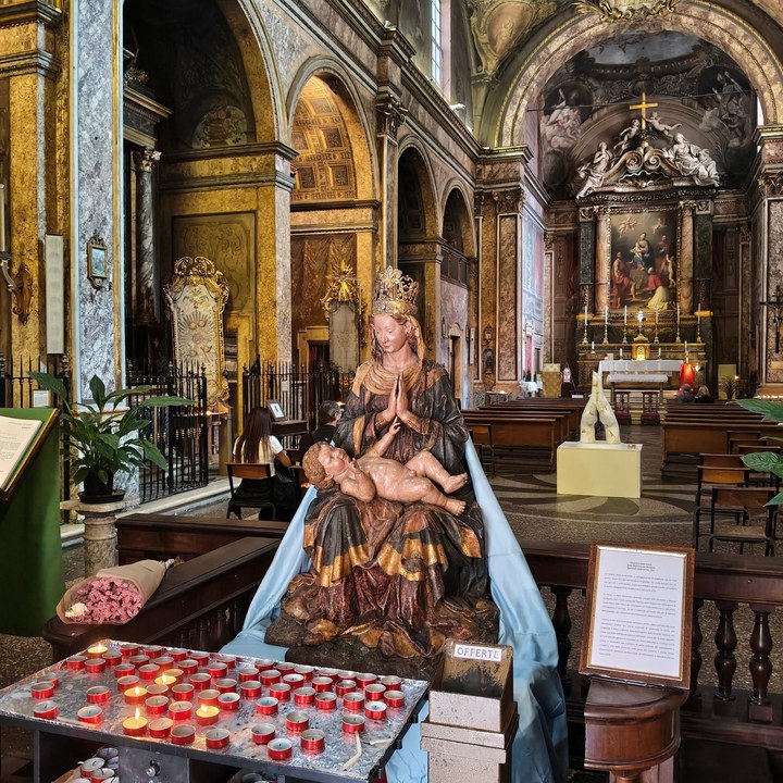 Madonna con il Bambino, lumini e cassetta delle offerte; sullo sfondo la navata e la scultura bianca di due mani giunte