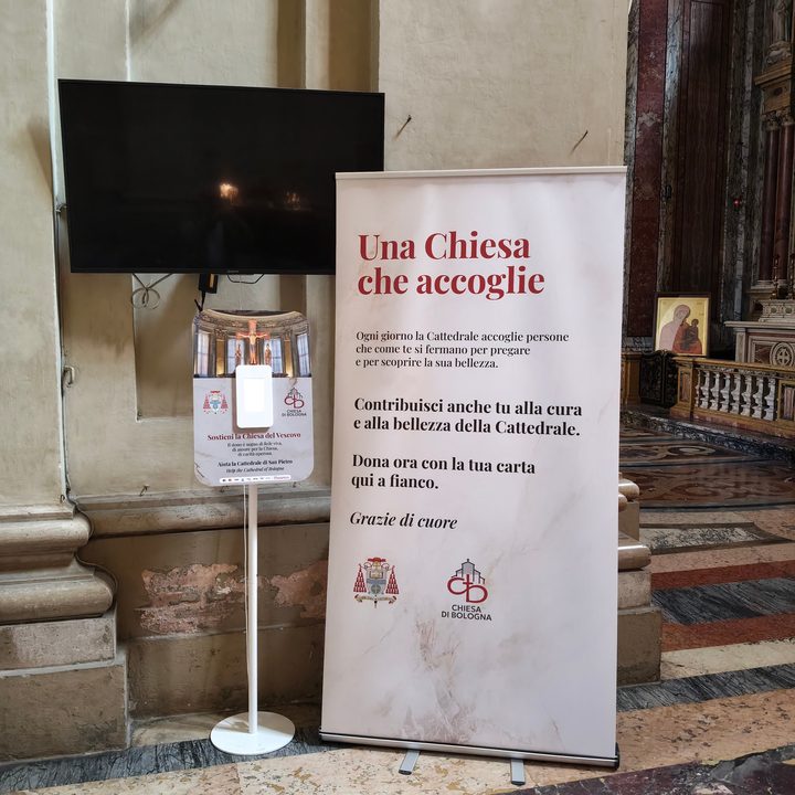 Un televisore spento e un totem per le donazioni accanto al pannello «Una Chiesa che accoglie»